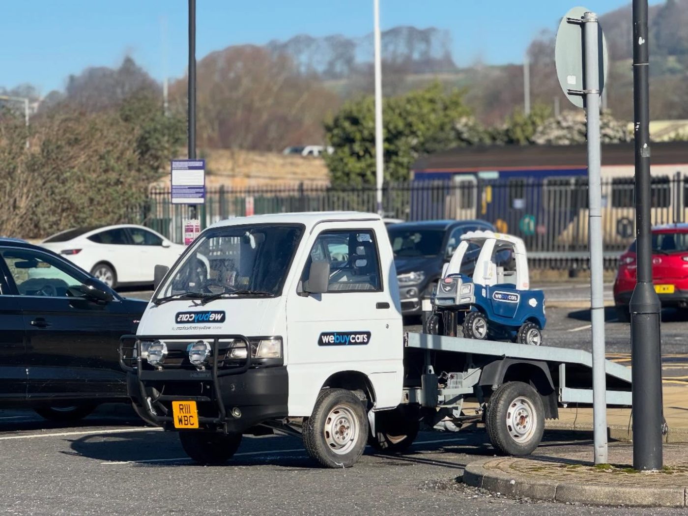 The tiny We Buy Cars recovery truck by Hexham railway station with a branded toy car on the back